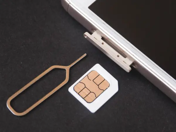 Narzędzie do otwierania tacki SIM i karta SIM obok telefonu. Dowiedz się, jak odblokować kartę SIM, aby móc korzystać z telefonu.