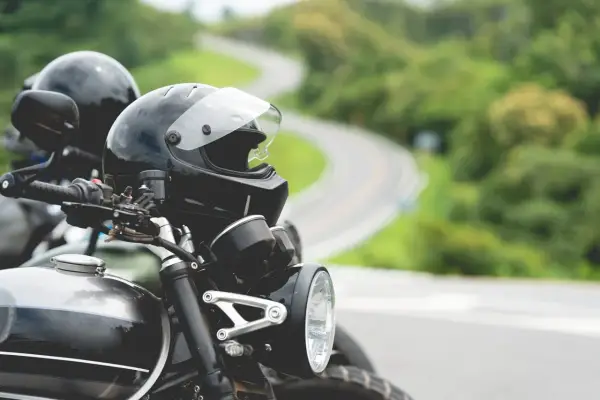 Gotowe na przygodę? Zastanawiasz się nad prawem jazdy na motor i wiekiem? Dwa kaski czekają na motocyklistów na krętej drodze.