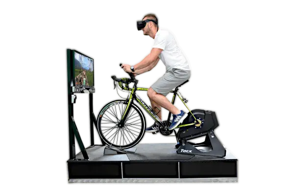 Mężczyzna w goglach VR pedałuje na rowerze stacjonarnym, doświadczając wirtualnej przejażdżki. To zaawansowany symulator jazdy rowerem.