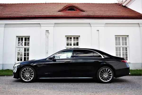 Elegancki, czarny Mercedes S500 lśni na tle białej, zabytkowej fasady z czerwonym dachem.