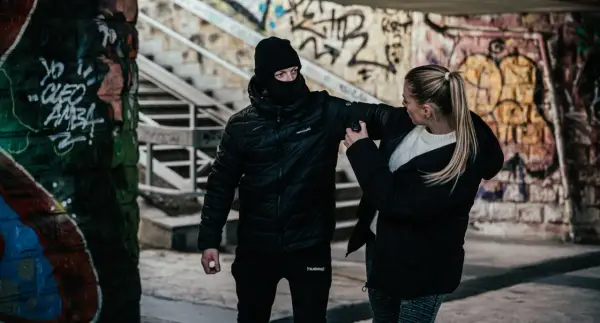 Kobieta używa gazu pieprzowego przeciwko napastnikowi w kominiarce. To przykład obrony koniecznej w niebezpiecznej scenerii z graffiti.