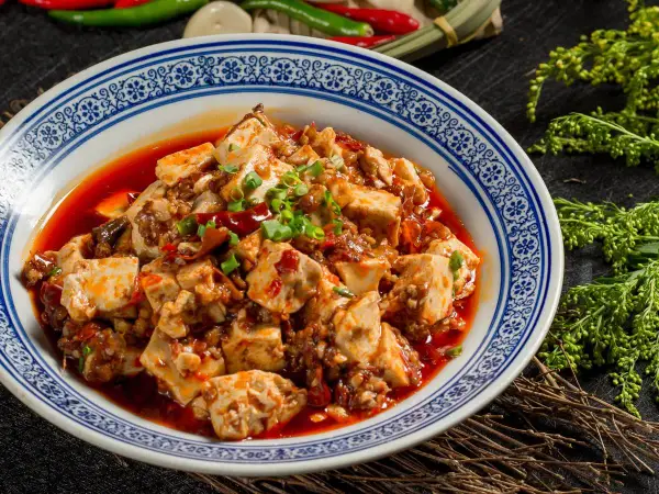 Pikantne tofu w sosie chili, klasyka kuchni syczuańskiej. Danie wygląda apetycznie, ozdobione szczypiorkiem.