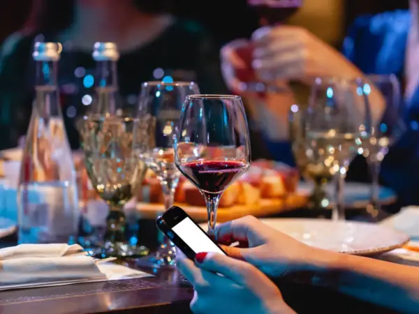 Zanim sięgniesz po alkohol, pomyśl o "podkładzie". Na stole wino, przekąski i telefon. Unikaj skutków picia alkoholu na pusty żołądek.