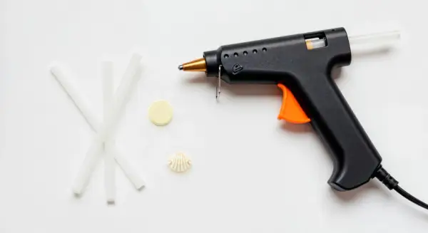 Pistolet do kleju na gorąco, kilka pałeczek kleju, muszelka i żółty krążek. Czy klej na gorąco przewodzi prąd?