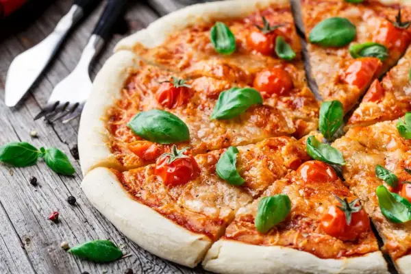 Pyszna pizza Margherita, klasyka włoskiego jedzenia, z pomidorkami koktajlowymi i bazylią na drewnianym blacie.
