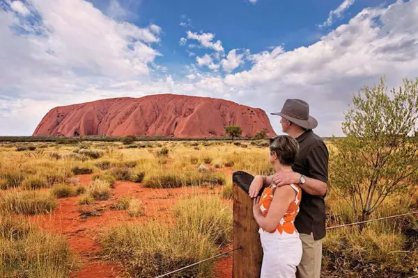 Para turystów podziwia Uluru, świętą skałę rdzennych mieszkańców Australii, w pustynnym krajobrazie.