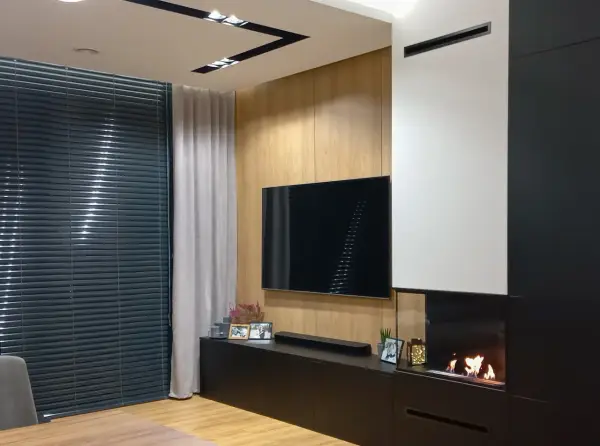Nowoczesny salon z telewizorem i palącym się kominkiem bio do zabudowy.