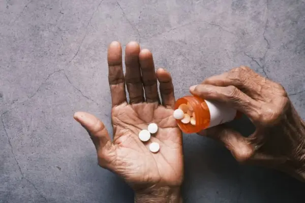 Dłoń wysypuje tabletki Tylenol z pomarańczowej buteleczki.