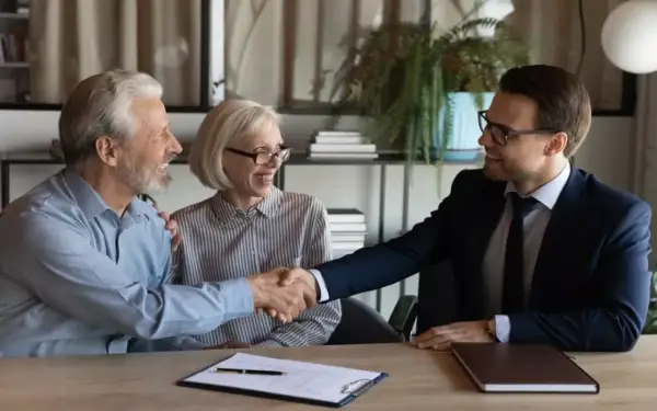 Un couple âgé serre la main d'un homme en costume. Ils sont co-emprunteurs mais pas propriétaires, un accord financier est signé.