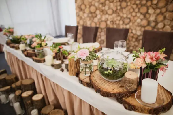 Festlich gedeckter Tisch mit Holzdeko und Blumen. Ein Terrarium und Kerzen unterstreichen die Bedeutung des 5. Hochzeitstags.