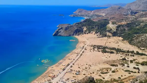 Rodos: turkusowe morze, piaszczysta plaża z leżakami i wodnym parkiem rozrywki, górzyste wybrzeże.