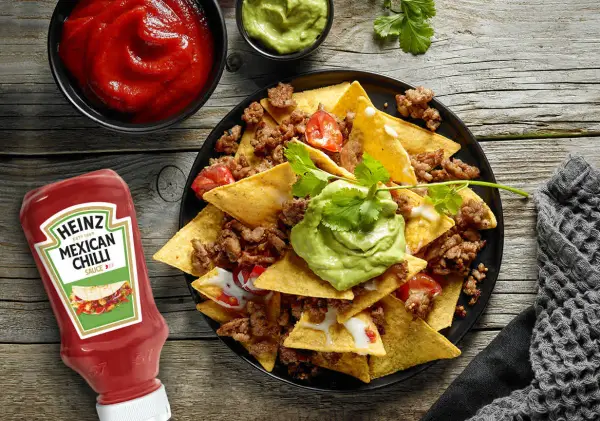 Nachos con carne, guacamole y salsa en un plato negro, con botella de Heinz y cuencos de salsa.