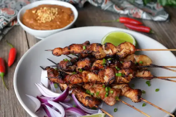 Pyszne satay z kurczaka na patyczkach, podane z sosem orzechowym, limonką i papryczkami chili.