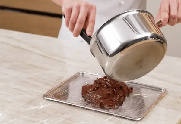 Comment faire fondre du chocolat : une casserole verse du chocolat fondu sur une plaque recouverte de film plastique.