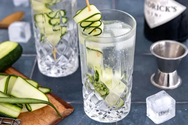 Erfrischendes Gin Tonic Rezept mit Gurke: Eisgekühlte Gläser, frische Gurkenscheiben und eine Flasche Gin.