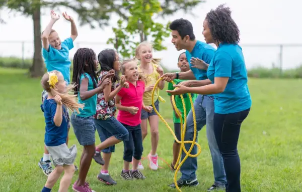 Des enfants et des animateurs jouent à la corde à sauter dans un parc.