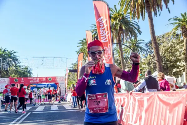 Lächelnder Läufer mit Medaille und rotem Kopftuch feiert seinen Erfolg beim Malaga Marathon.