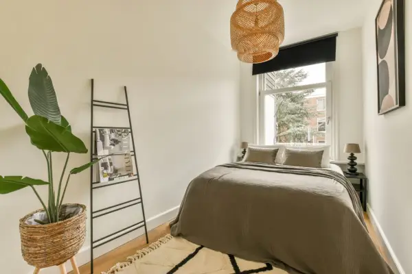 Chambre 9m2 avec salle de bain, lit douillet, plante verte et étagère murale. Luminaire en rotin au-dessus.