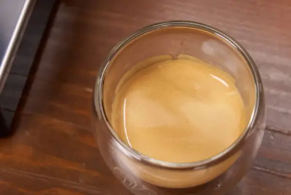 Ein Glas Espresso mit einer feinen Crema auf einem Holztisch. Ein kleiner Schuss Sahne macht den Kaffee mit Sahne gesund und lecker.