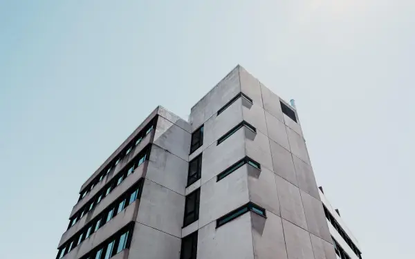 Betonowy budynek o geometrycznej bryle, z rzędami okien. Ta kategoria obiektu budowlanego dominuje w kadrze.