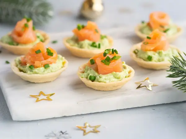 Aperitivos baratos para mucha gente: canapés de salmón y aguacate, decorados con cebollino y estrellas doradas.