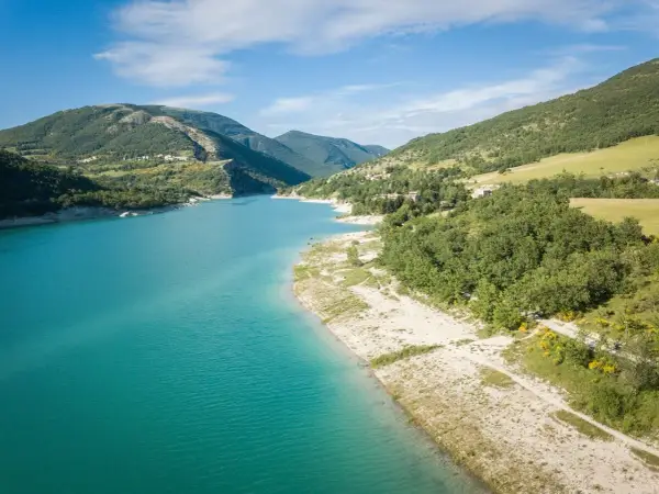 Splendido **lago di Fiastra** con acque turchesi, circondato da colline verdi e case sparse. Un paesaggio sereno e incantevole.