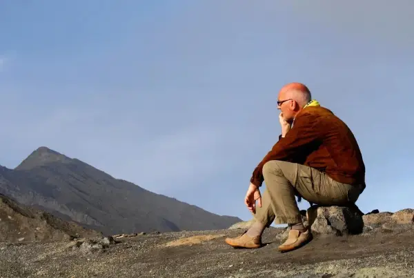 A man in hiking gear sits on a rock, contemplating the vast, barren landscape. This is the essence of zero day hiking, a moment of quiet reflection before the real adventure begins.