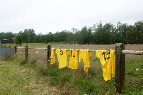 Maillots de foot jaunes floqués, numéros 5, 10, 12, sèchent sur une barre rouillée. Une astuce pour savoir comment laver un maillot de foot floqué.