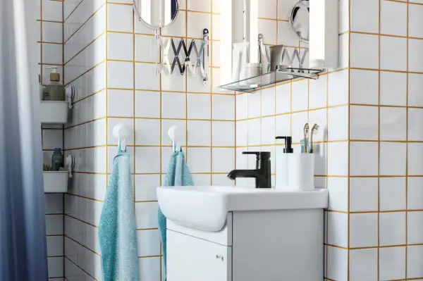 Salle de bain moderne avec carrelage blanc joint gris, lavabo, robinetterie noire et accessoires pratiques.