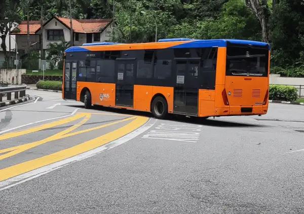 Pomarańczowo-niebieski autobus miejski na zakręcie drogi z żółtymi pasami.