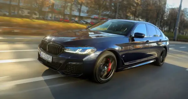 Ciemnoniebieskie BMW 540d sunie po drodze, odbijając jesienne słońce.