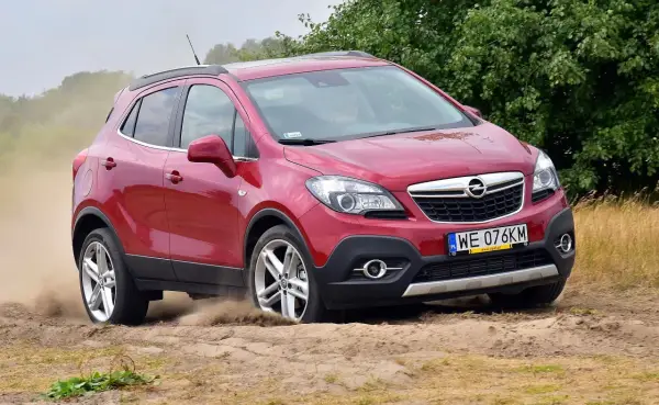 Czerwony Opel Mokka 1.4 Turbo z napędem na cztery koła pokonuje piaszczysty teren, wzbijając tumany kurzu.