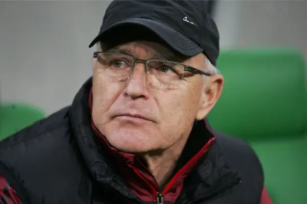 Lenczyk, trener piłkarski, w okularach i czapce, z uwagą obserwuje grę.