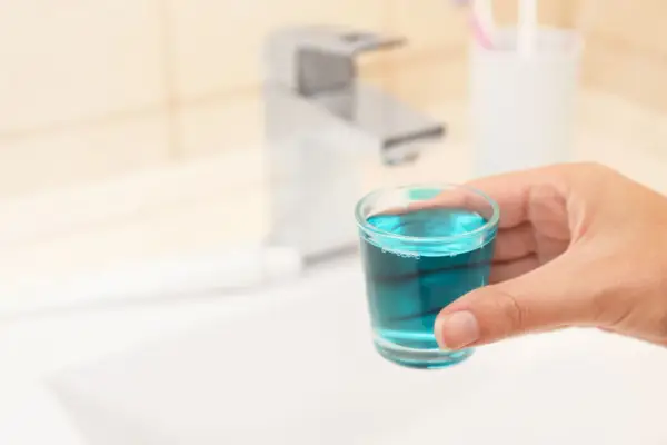 Mano tiene bicchierino con collutorio azzurro, ideale per l'igiene orale in gravidanza.