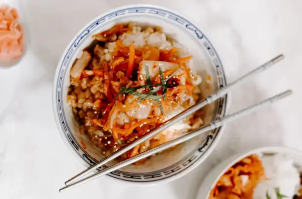Miseczka ryżu z pikantnym kimchi i marchewką, idealne połączenie. Pałeczki czekają, by zacząć jeść.