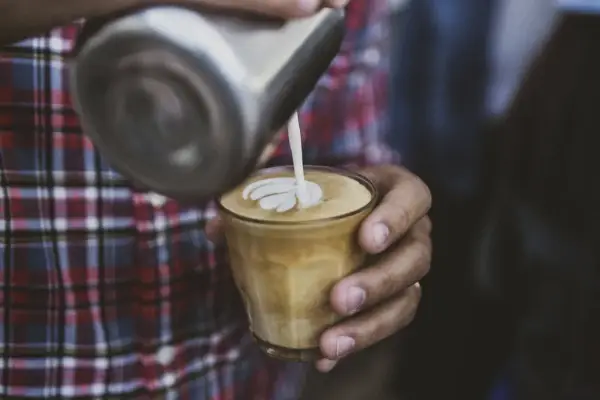 Barista wylewa mleko z dzbanka, tworząc wzór na kawie. To właśnie zabielacz do kawy, który nadaje jej kremową konsystencję i piękny wygląd.