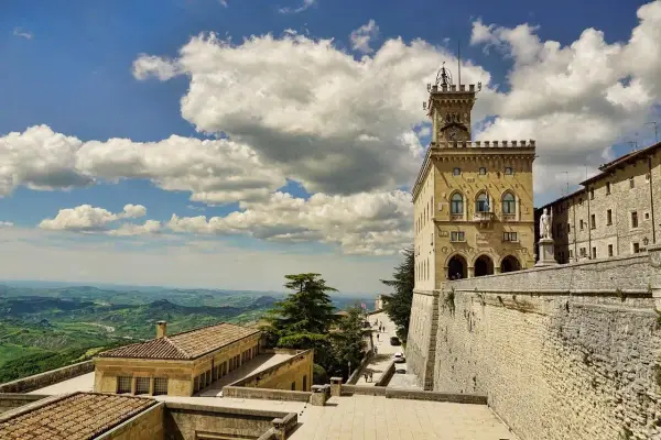 Torre del Campanone e Palazzo Pubblico nel **San Marino centro**, con vista panoramica sulle colline verdi sotto un cielo azzurro e nuvoloso.