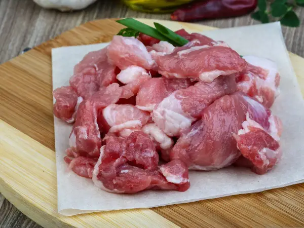 Surowe, pokrojone w kostkę mięso wieprzowe, idealne na gulasz. W tle czosnek i papryczki chili.