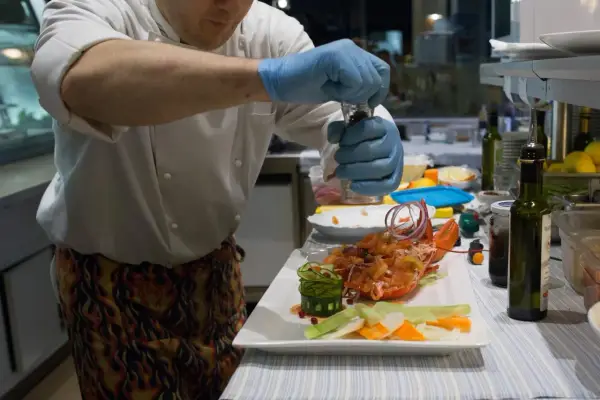 Chef con guanti blu macina pepe su un'aragosta, un piatto che sembra uscito da "lo zodiaco Rimini".