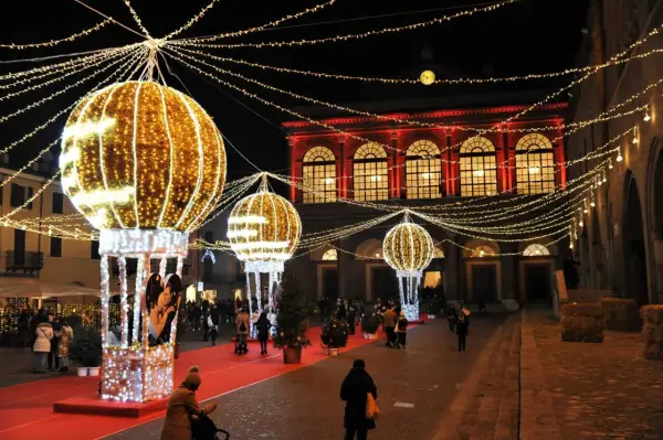 Luci scintillanti e palloni luminosi creano un'atmosfera magica per un week end a Rimini. Persone passeggiano su un tappeto rosso, ammirando le decorazioni natalizie.