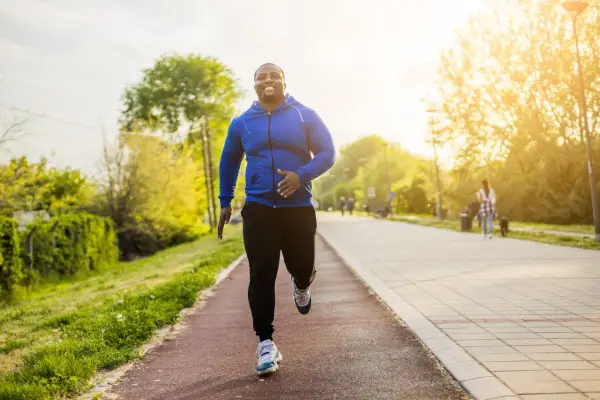 Glücklicher Mann beim Laufen im Park. Sein Training laufen im Sonnenschein macht ihn fit und gesund.