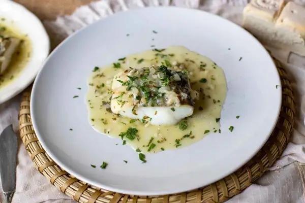 Un delicioso bacalao en salsa verde, con perejil fresco picado y trozos de pan al lado.