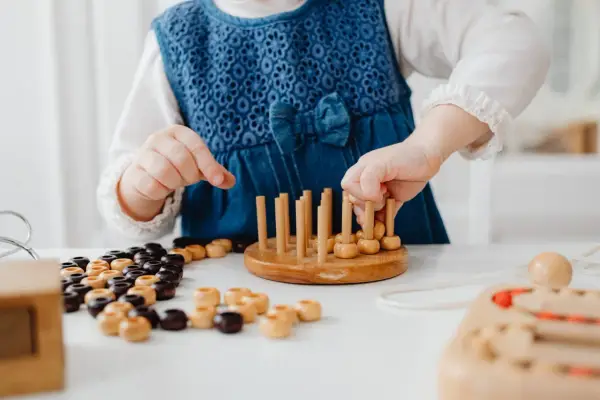 Niña con vestido azul jugando con cuentas de madera y un juego de encaje, parte de juegos para superar el mutismo selectivo.