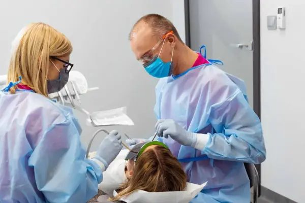 Znieczulenie u dentysty w ciąży. Dwoje stomatologów w fartuchach i maskach wykonuje zabieg u pacjentki.