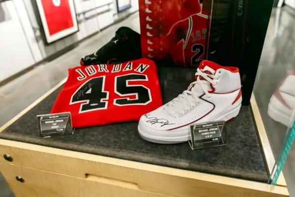 Białe buty sportowe z czerwonymi akcentami, podpisane przez Michaela Jordana, obok koszulki z numerem 45. To pamiątki, które pokazują, jaki michael jordan rozmiar buta nosił.