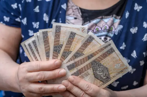 Dłonie trzymające kilka banknotów po 200 zł. Czy to przyszłość renty wdowiej? Zmiany w przepisach mogą wpłynąć na finanse.