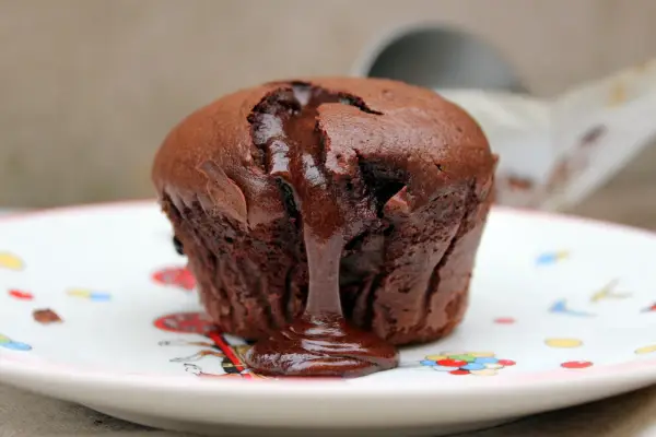 Coulant de chocolate tibio con centro líquido, servido en un plato blanco con dibujos de colores.