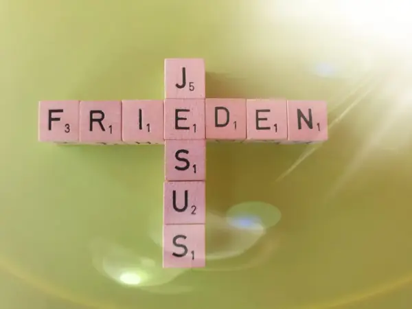 Buchstabensteine bilden ein Kreuz mit den Wörtern "FRIEDEN" und "JESUS". Ein Zitat aus Johannes 14.