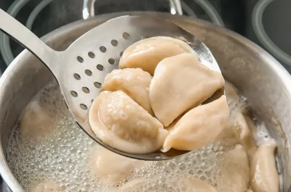 Gorące pierogi z serem, gotowane według przepisu babci, wyjmowane łyżką cedzakową z bulgoczącego garnka.