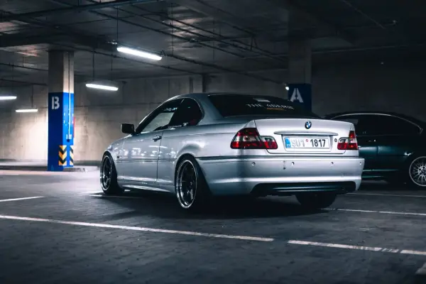 Srebrne BMW serii 3 (m54) z przyciemnianymi szybami i czarnymi felgami stoi na parkingu podziemnym.
